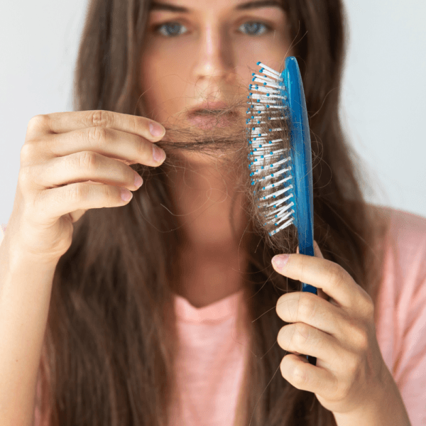Mujer con cabello largo mirando preocupada un cepillo lleno de pelo, ilustrando la caída capilar y la importancia de los champús anticaída para prevenirla