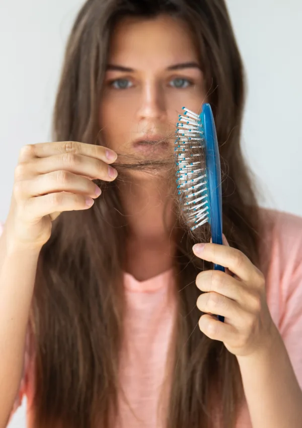 Mujer con cabello largo mirando preocupada un cepillo lleno de pelo, ilustrando la caída capilar y la importancia de los champús anticaída para prevenirla