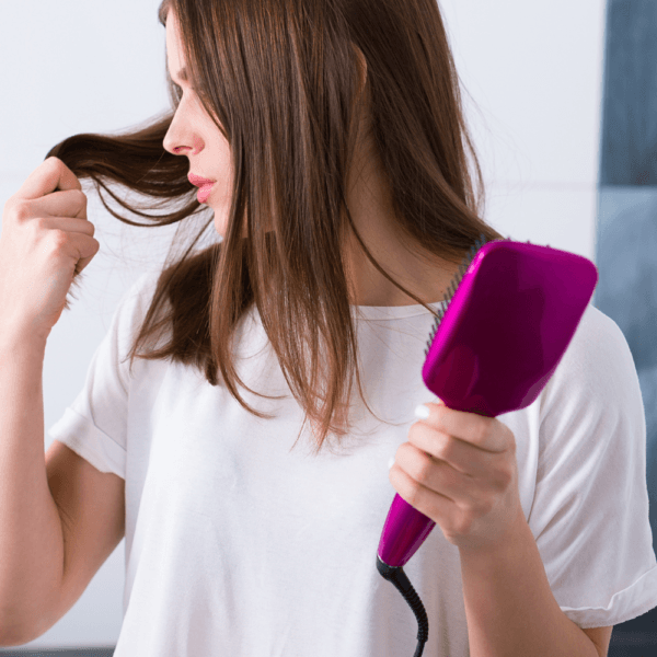 Mujer utilizando cepillos alisadores eléctricos de color rosa mientras examina un mechón de su cabello.