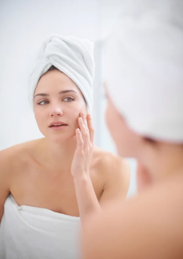 Mujer aplicando productos de cuidado facial como parte de su rutina Skin Cycling, envuelta en una toalla blanca