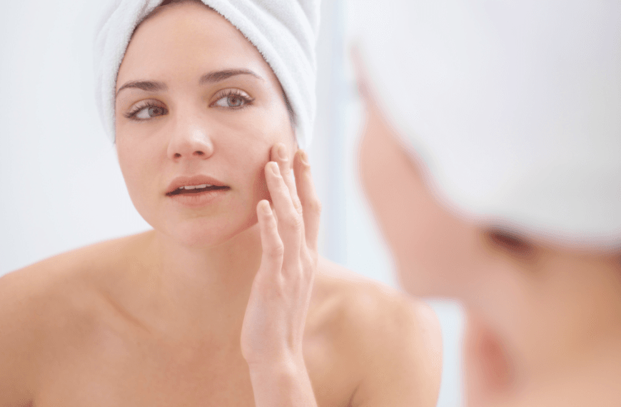 Mujer aplicando productos de cuidado facial como parte de su rutina Skin Cycling, envuelta en una toalla blanca