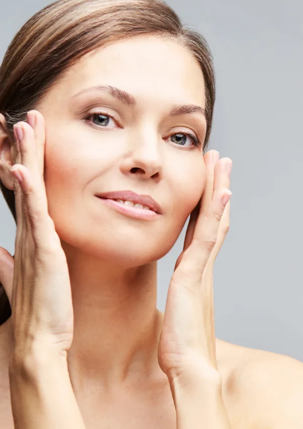 Mujer con piel madura cuidando su rostro, aplicando un tratamiento facial con las manos, mostrando una piel luminosa y saludable