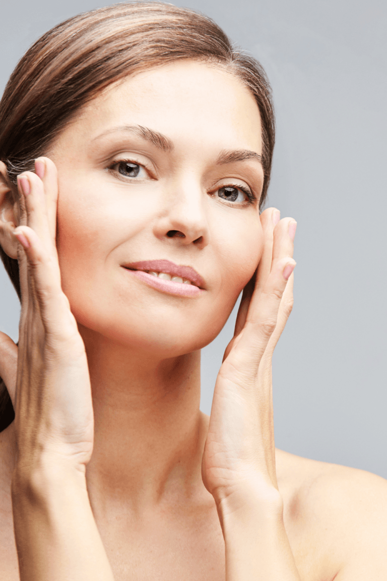 Mujer con piel madura cuidando su rostro, aplicando un tratamiento facial con las manos, mostrando una piel luminosa y saludable