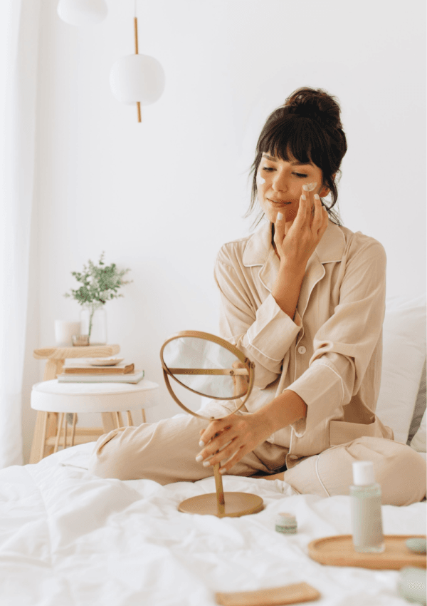 Cómo Combinar Ingredientes Activos . Mujer aplicándose crema en el rostro sentada en su cama como parte de su rutina de skincare