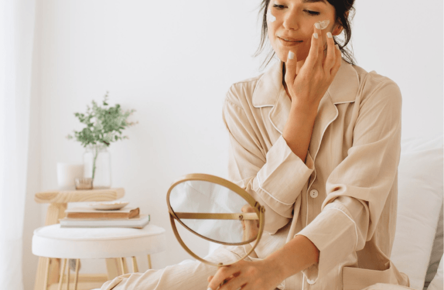 Cómo Combinar Ingredientes Activos . Mujer aplicándose crema en el rostro sentada en su cama como parte de su rutina de skincare