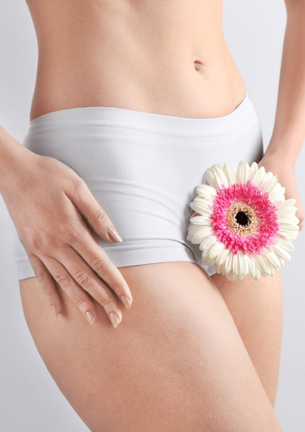 Mujer con ropa interior blanca sosteniendo una flor rosa y blanca sobre su cadera, con fondo claro.