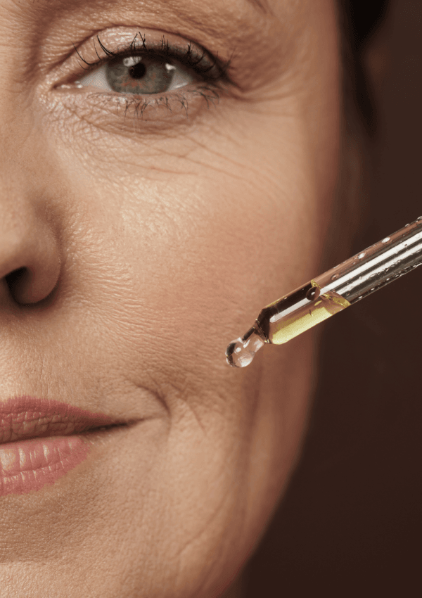 Mujer madura aplicando aceite facial con un gotero en su piel para hidratar y nutrir el rostro.