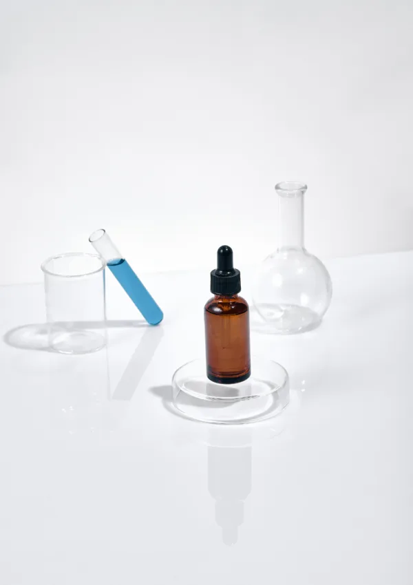 Frasco de suero cosmético con factores de crecimiento en cosmética, rodeado de tubos de ensayo y matraces en un fondo blanco minimalista